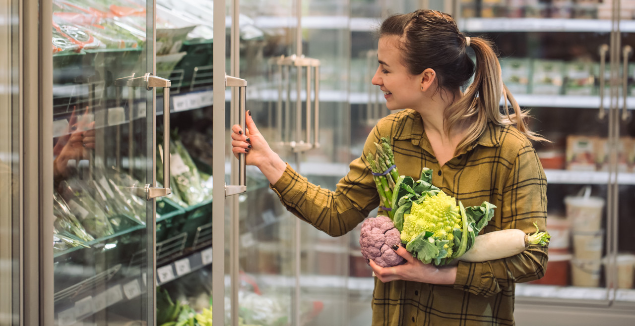Woman in the supermarket. Beautiful young woman holds in hands fresh organic vegetables and opens the fridge in the supermarket. The concept of healthy eating. Harvest