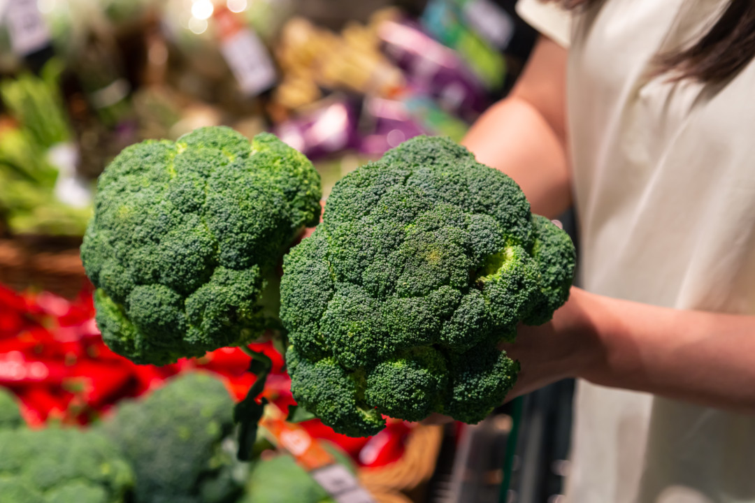Woman chooses broccoli, buying vegetables in supermarket. Concept of shopping groceries and healthy lifestyle.